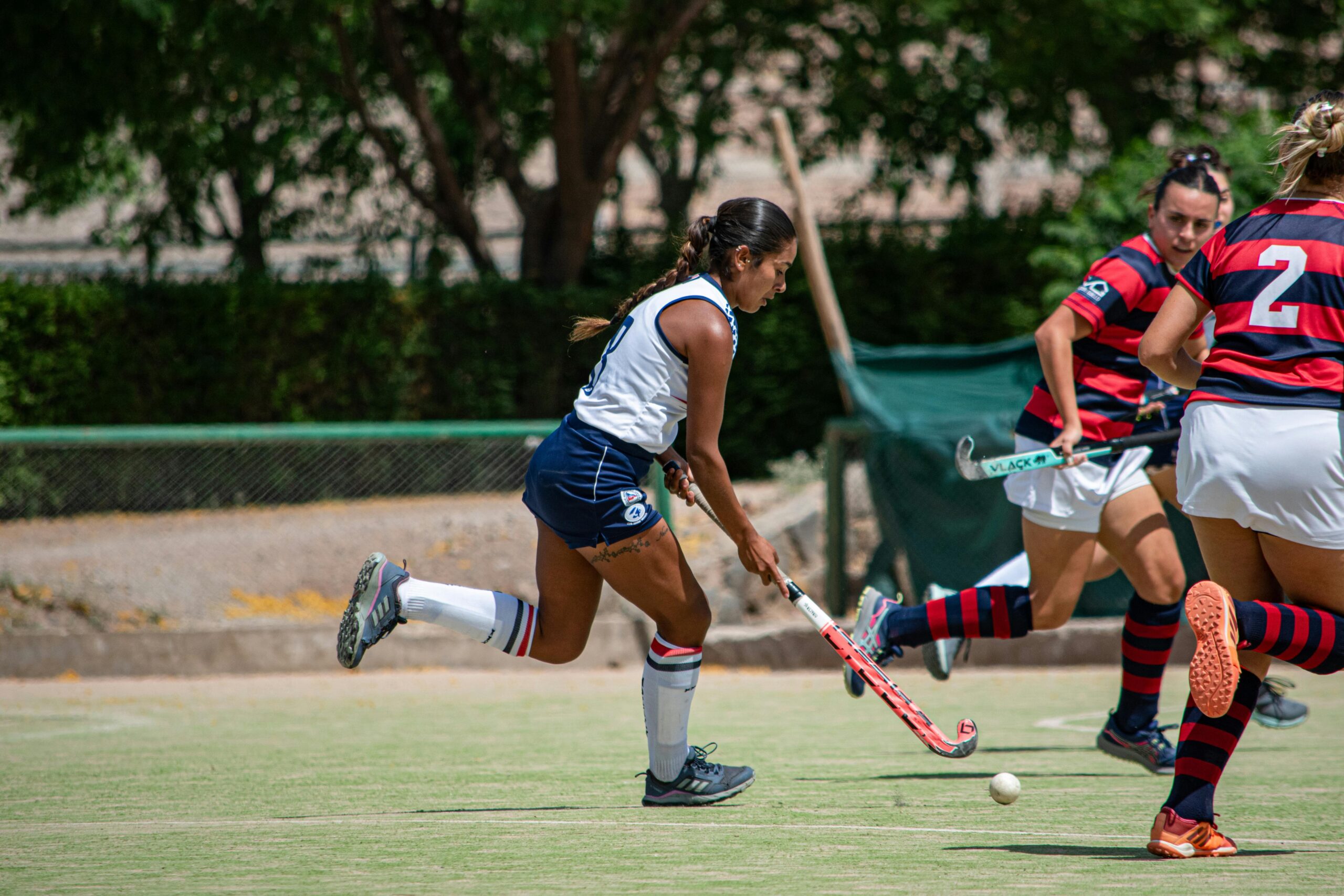 Dynamic action shot of female field hockey players competing outdoors on a sunny day.