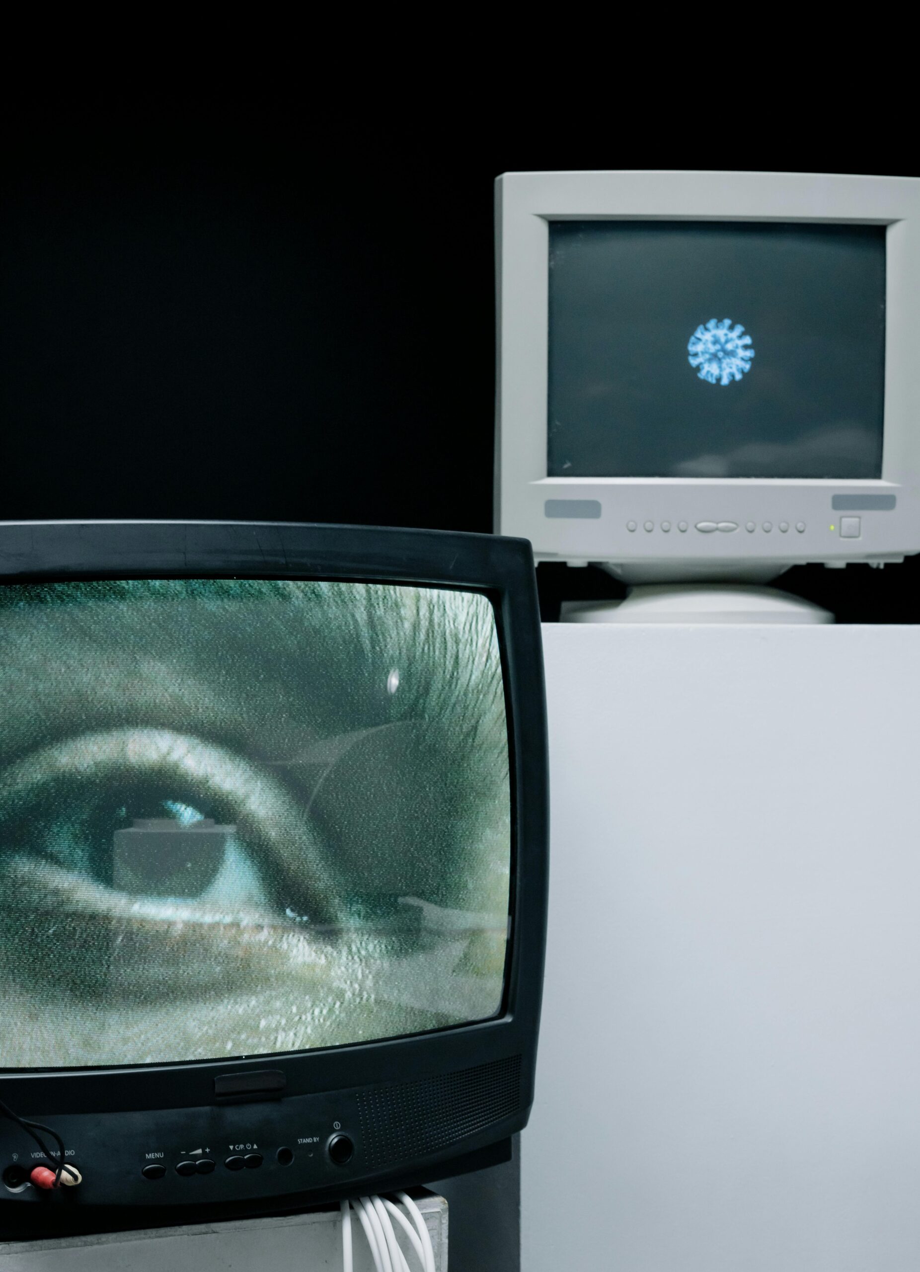 Retro TV and computer monitor showing eye and virus image, depicting surveillance and medical research themes.