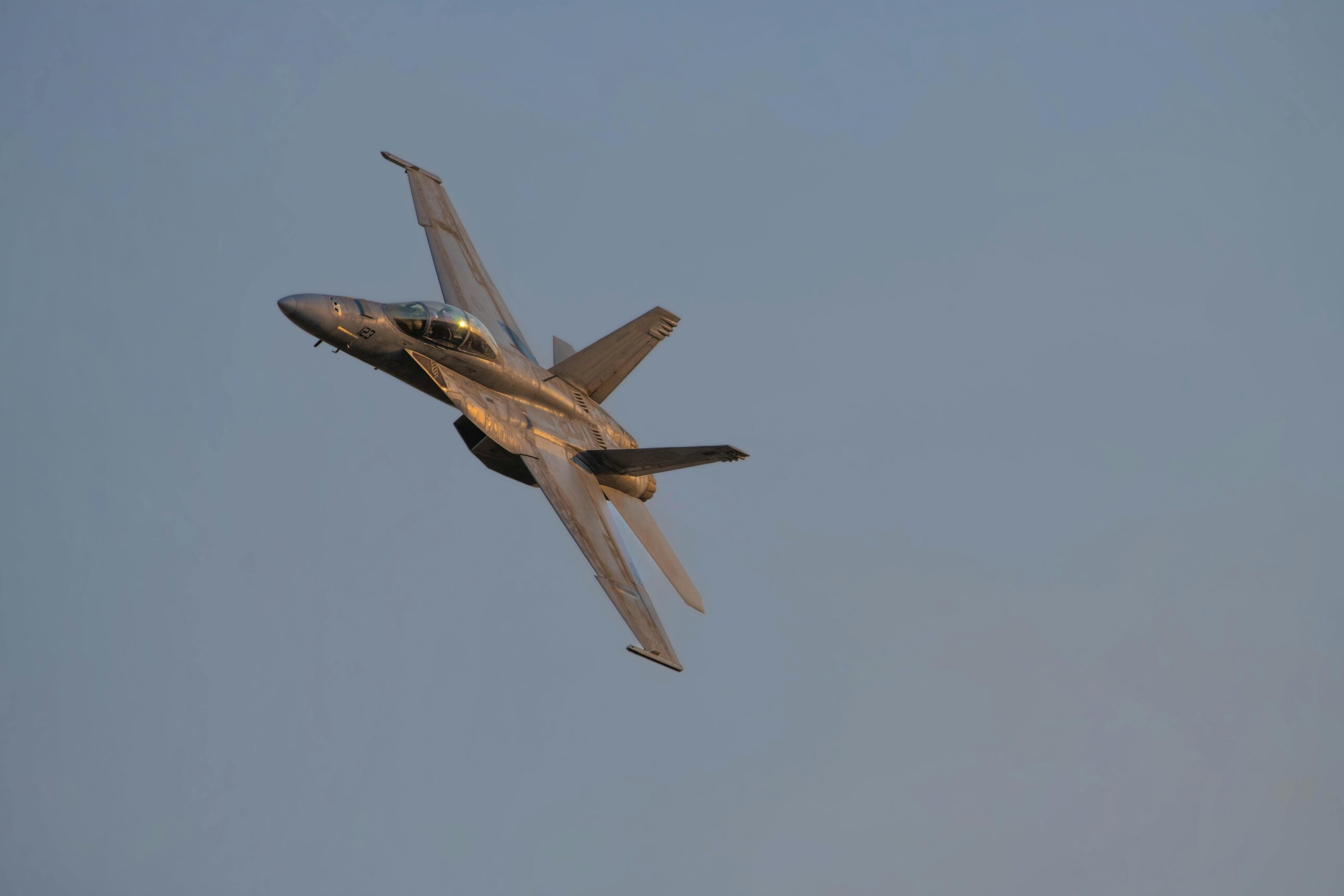 A military jet performing an aerobatic maneuver in clear skies during dusk light.