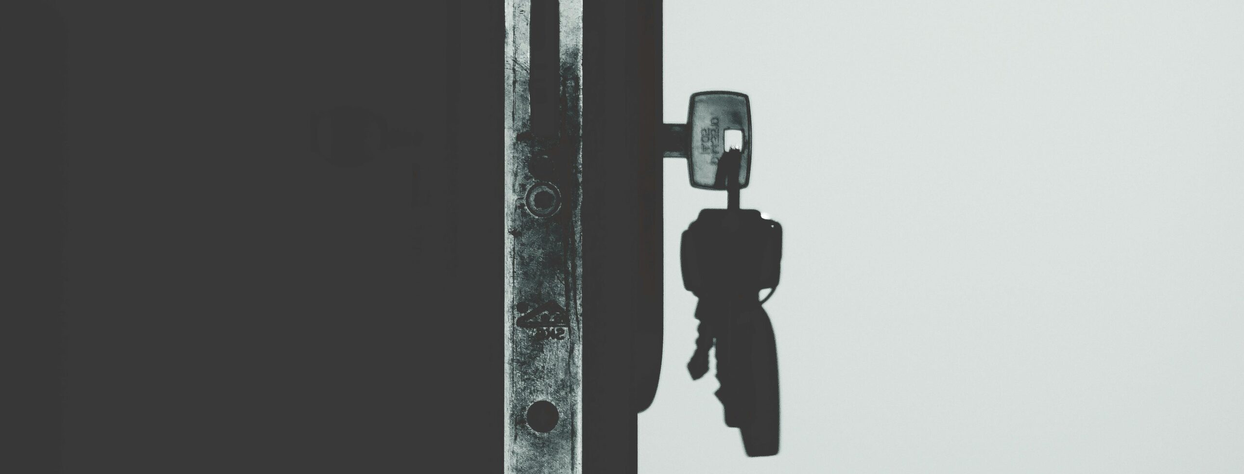 Black and white image showcasing a door lock with a key inserted, casting shadows.